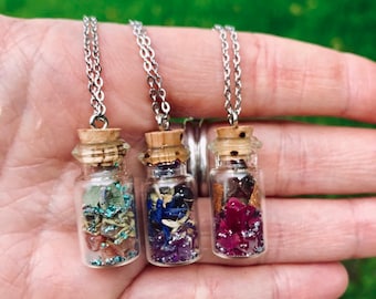 May include: Three silver chain necklaces with small glass bottles filled with colorful crystals and glitter. The bottles have cork stoppers.