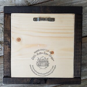 May include: The back of a wooden sign with a dark brown frame. The sign has a black stamp that says "Hand Painted by Little Rustic Sign Shoppe" with a website and email address.