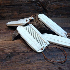 May include: Ivory-coloured combs and hair accessories with leather cords are displayed on a wooden surface. The combs have a rectangular shape with teeth and decorative carvings. The Viking Thunder logo is visible in the upper left corner.