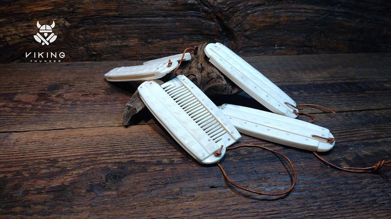 May include: Ivory-coloured combs and hair accessories with leather cords are displayed on a wooden surface. The combs have a rectangular shape with teeth and decorative carvings. The Viking Thunder logo is visible in the upper left corner.