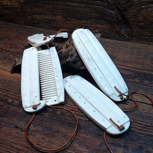 May include: Ivory-coloured Viking-style combs and accessories with leather cords, displayed on a dark wooden surface. The combs have carved details and are arranged with a logo that says "VIKING THUNDER".