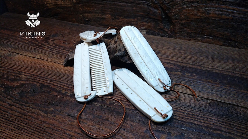 May include: Ivory-coloured Viking-style combs and accessories with leather cords, displayed on a dark wooden surface. The combs have carved details and are arranged with a logo that says "VIKING THUNDER".