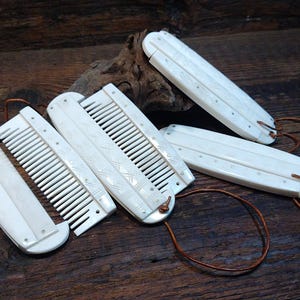 May include: Ivory-coloured Viking combs with detailed carvings and leather cords. The combs are arranged on a dark wooden surface, highlighting their intricate design and craftsmanship. The Viking Thunder logo is in the upper left corner.