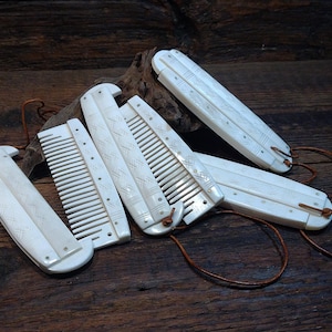 May include: A collection of off-white combs with intricate designs and leather cords, arranged on a dark wooden surface. The combs vary in size and shape, showcasing a rustic, handcrafted aesthetic. The Viking Thunder logo is visible in the upper left corner.