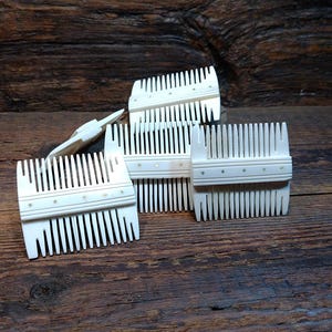 Puede incluir: Cuatro peines blancos con detalles decorativos, dispuestos sobre una superficie de madera. Los peines tienen una forma rectangular y están hechos de un material blanco liso.