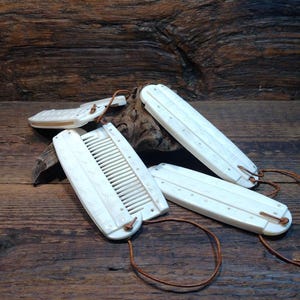 May include: Several white combs and grooming tools with leather straps, displayed on a rustic wooden surface. The Viking Thunder logo is in the top left corner. The combs are rectangular in shape.