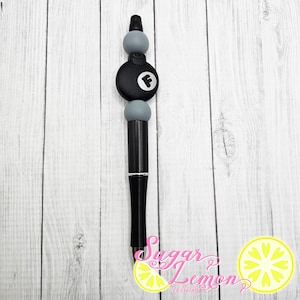 May include: Black pen with a gray and black 8-ball design. The 8-ball has a white "F" on it.