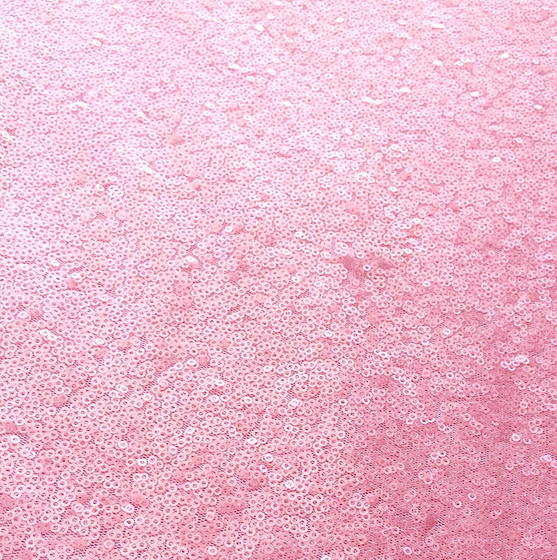 Op de afbeelding: Close-up van een roze paillettenstof. De pailletten zijn klein, rond en dicht op elkaar gepakt, waardoor een glinsterend, gestructureerd oppervlak ontstaat. De kleur is een zacht, lichtroze, met tintvariaties. Deze stof is geschikt voor kleding en decoratieve projecten.