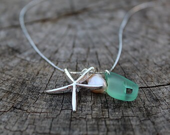 May include: A silver chain necklace with a silver starfish charm, a pearl, and a light green sea glass charm.
