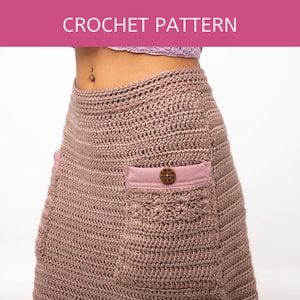 Può includere: Una gonna a uncinetto di colore rosa polvere con due tasche e un bottone di legno sul lato destro.
