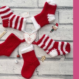 May include: Four crocheted Christmas stockings in red and white stripes. Two stockings are solid red, and two are red and white striped. The stockings are arranged in a circle on a white brick background.