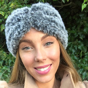 May include: A gray faux fur headband with a twisted design. The headband is worn by a person with long blonde hair.