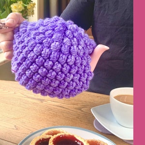 Może przedstawiać: Fioletowy, dziergany na szydełku ochraniacz na czajnik z fakturowanym wzorem w postaci kuleczek. W tle widoczny jest tekst CROCHET PATTERN.