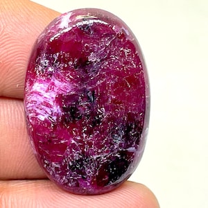 Op de afbeelding: Een grote, ovale, cabochon geslepen, roze robijn met een donker, swirlend patroon en een hoge glans.