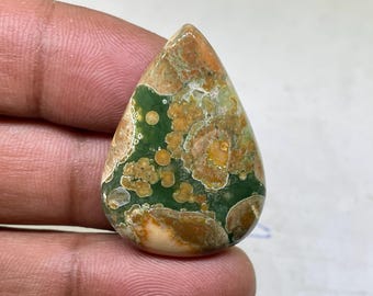 May include: A teardrop-shaped green, brown, and white jasper cabochon with a unique pattern of swirls and dots.