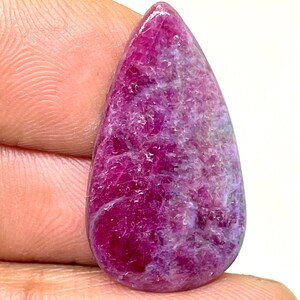 Może przedstawiać: Kamień szlachetny w kształcie łzy, w kolorze różowym i fioletowym. Kamień szlachetny ma szorstką, fakturowaną powierzchnię.