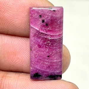 May include: A rectangular pink and black gemstone cabochon with a wavy pattern.