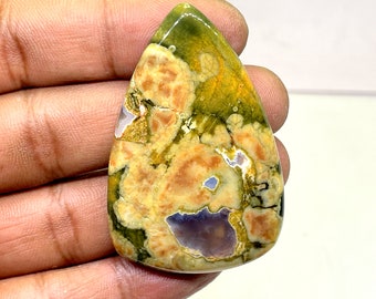May include: A teardrop-shaped cabochon of green, yellow, and white ocean jasper. The stone has a unique, swirling pattern.