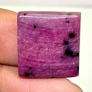 Op de afbeelding: Een vierkante, roze edelsteen met zwarte insluitsels. De edelsteen is geslepen en gepolijst en heeft een glad, glanzend oppervlak.