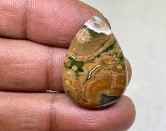 May include: A teardrop-shaped cabochon of brown, green, and white patterned agate. The stone has a smooth, polished surface.