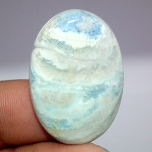 May include: Oval cabochon gemstone with a blue and white swirling pattern. The stone has a translucent appearance and a smooth, polished finish.