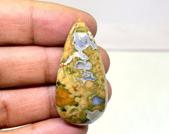 May include: A teardrop-shaped cabochon of green, yellow, and white ocean jasper. The stone has a swirling, abstract pattern.