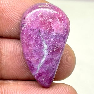 Puede incluir: Una piedra preciosa rosa y púrpura pulida en forma de lágrima con vetas blancas.