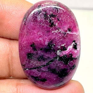 以下が含まれることがあります： 鮮やかなマゼンタ色の楕円形の宝石で、黒いインクルージョンが散りばめられています。研磨された表面は光を反射し、石の自然な模様と質感を際立たせています。天然鉱物の美しさを示す素晴らしい例です。約3cm。