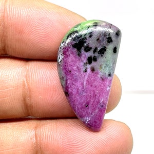 Może przedstawiać: Różowo-zielony kaboszon z czarnymi inkluzjami. Kamień szlachetny jest oszlifowany w kształcie łzy.