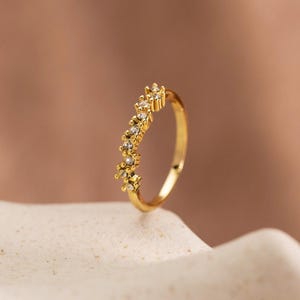 May include: A gold ring featuring a curved, cluster-style band set with multiple small, clear, round-cut stones arranged in a delicate, asymmetrical pattern along the top half of the circular metal band, creating a sparkling, textured appearance.