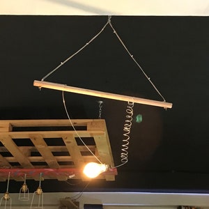 Puede incluir: Una bombilla colgando de una barra de madera suspendida por una cuerda del techo. La barra está unida a una paleta de madera.