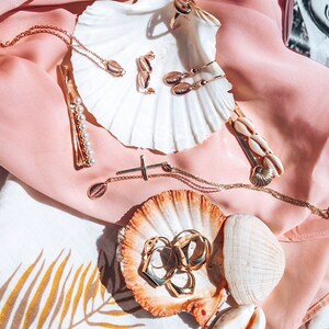 May include: A collection of gold jewelry featuring seashell designs, displayed on seashells. The jewelry includes a necklace, earrings, rings, and a hair clip.
