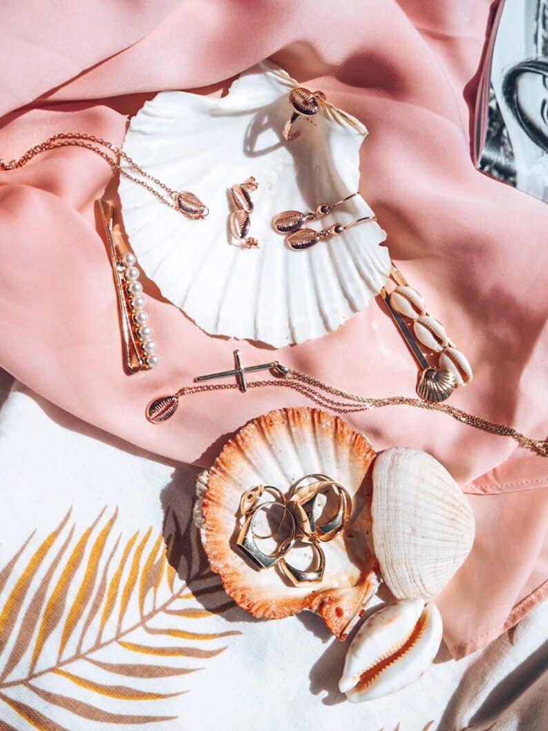 May include: A collection of gold jewelry featuring seashell designs, displayed on seashells. The jewelry includes a necklace, earrings, rings, and a hair clip.