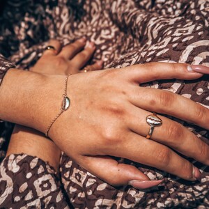 May include: A gold chain bracelet with a small seashell charm and a gold ring with a seashell design.