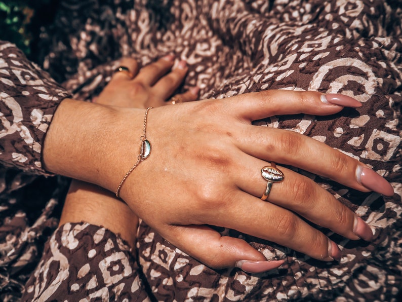 May include: A gold chain bracelet with a small seashell charm and a gold ring with a seashell design.
