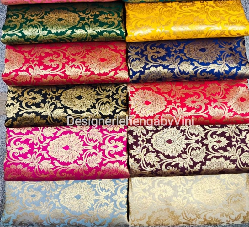 Pu&ograve; includere: Un set di campioni di tessuto di diversi colori e motivi. Il tessuto &egrave; in broccato con un disegno in filo d'oro. I campioni di tessuto sono disposti in fila, con il campione superiore rosa, il secondo verde, il terzo giallo, il quarto blu, il quinto rosso, il sesto nero, il settimo rosa, l'ottavo marrone, il nono azzurro e il decimo beige. Il testo "DesignerlehengabyVini" &egrave; visibile sui campioni di tessuto.