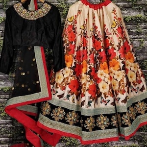 Pu&ograve; includere: Un lehenga con stampa floreale bianco e nero con una blusa ricamata nera e un dupatta in rete nera. Il lehenga ha un bordo rosso e la blusa ha un collo con perline.