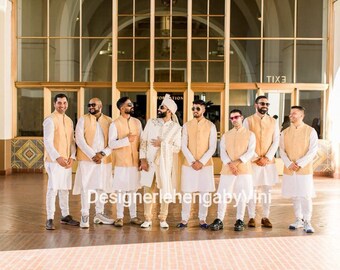 May include: A group of men wearing white kurtas and beige vests stand in front of a building with large windows. They are all smiling and looking at the camera. The men are wearing traditional Indian clothing.