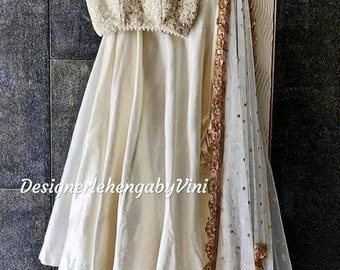 May include: Ivory-colored lehenga set, featuring a beaded crop top with spaghetti straps and a flowing skirt. A sheer dupatta with gold sequin trim and accents completes the ensemble. The text "DesignerlehengabyVini" is visible.