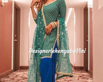 Può includere: Una donna indossa un salwar kameez verde acqua con ricami dorati e argentati. Il salwar kameez è abbinato a un salwar blu e a un dupatta verde acqua abbinato. Il dupatta ha un bordo dorato e argentato. La donna è in piedi in un corridoio con un tappeto a motivi.