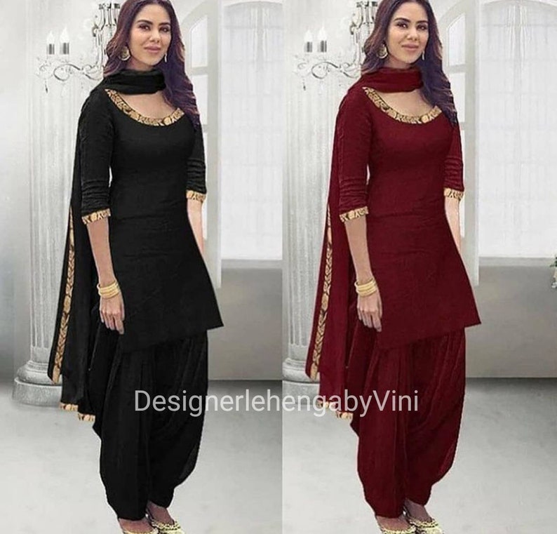 Pu&ograve; includere: Due donne che indossano abiti tradizionali indiani. La donna a sinistra indossa un salwar kameez nero con un bordo dorato. La donna a destra indossa un salwar kameez color granata con un bordo dorato. Entrambe le donne indossano gioielli d'oro e hanno i capelli tirati indietro. Il testo "DesignerlehengabyVini" &egrave; visibile nella parte inferiore dell'immagine.
