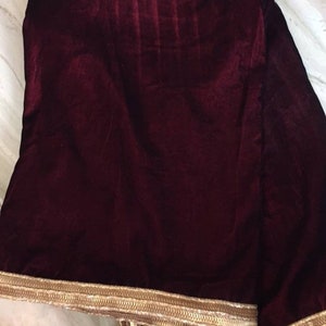 May include: A burgundy velvet shawl with a gold trim. The shawl is folded and the trim is visible on all sides.