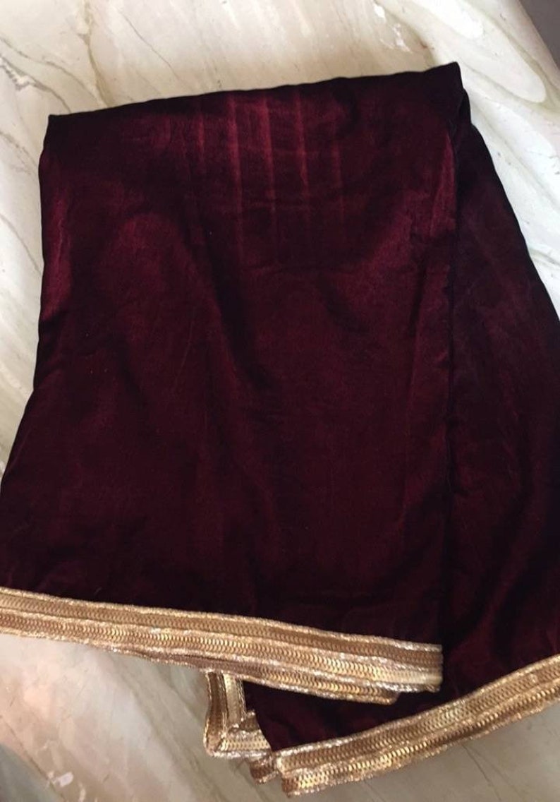 May include: A burgundy velvet shawl with a gold trim. The shawl is folded and the trim is visible on all sides.