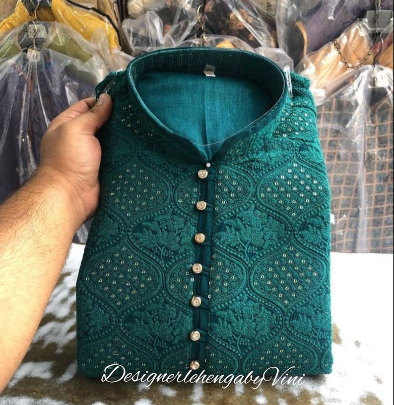 Puede incluir: Una kurta azul turquesa con un patr&oacute;n floral y botones dorados. La kurta tiene un cuello mandar&iacute;n y est&aacute; bordada con peque&ntilde;as lentejuelas.