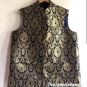May include: A black sleeveless vest with a gold brocade pattern. The vest has a mandarin collar and a button closure. The vest has two pockets on the front.
