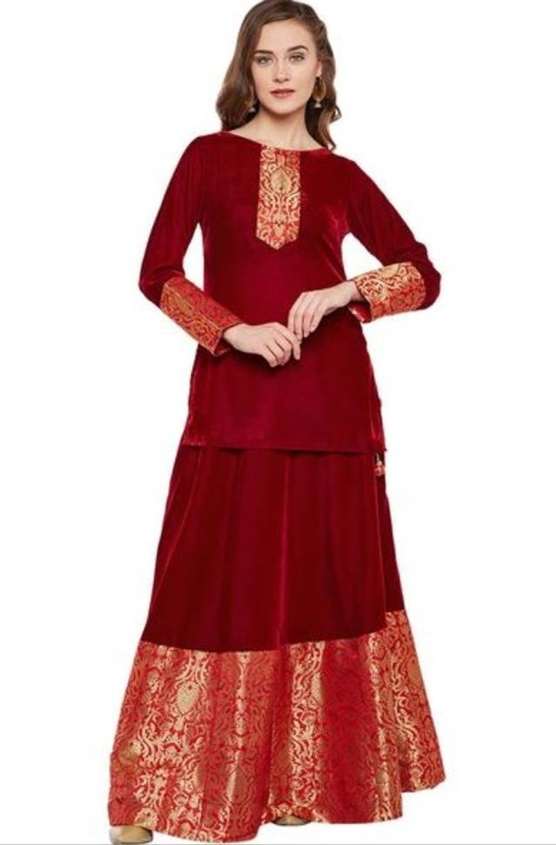May include: A maroon velvet kurta and skirt set with gold embroidery. The sleeves and bottom of the skirt have a gold and red brocade trim.
