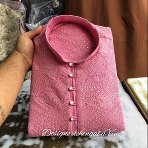 Puede incluir: Una kurta rosa con cuello alto y bordados intrincados. La kurta tiene cierre de botones y est&aacute; decorada con peque&ntilde;as cuentas blancas. El texto "DesignerlehengabyVini" es visible en la parte inferior de la imagen.