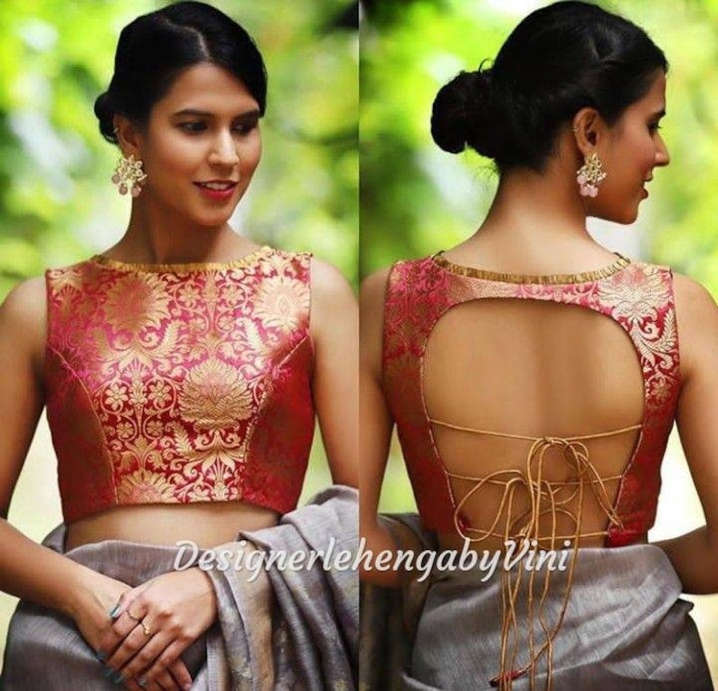 May include: A red and gold brocade sleeveless blouse with a round neckline and a keyhole back with a lace-up detail. The blouse is worn by a person with their back to the camera.