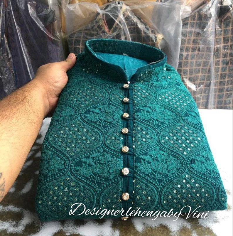 Puede incluir: Una kurta azul turquesa con cierre de botones en la parte delantera y bordados intrincados. La kurta tiene un cuello alto y est&aacute; decorada con peque&ntilde;as lentejuelas plateadas.