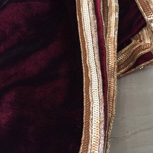 May include: A burgundy velvet shawl with a gold and silver sequined trim.